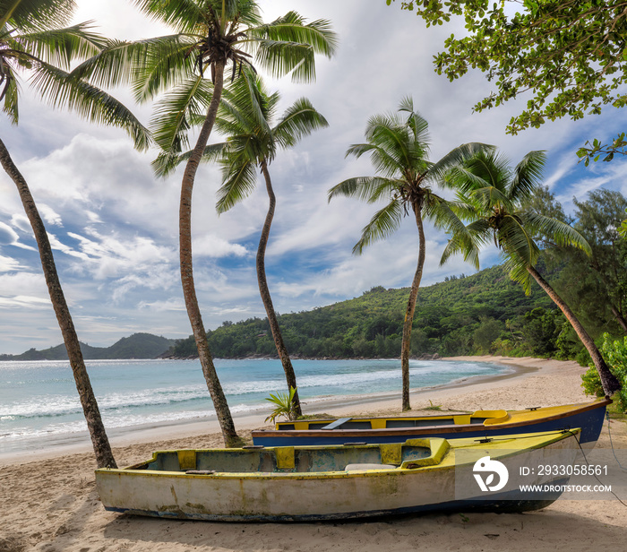 Exotic tropical beach with coco palm trees and a fishing boats in the turquoise sea on Paradise island.