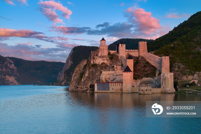 Aerial view over the water of medieval fortress Golubac illuminated by pink light of setting sun. Traveling Serbia.