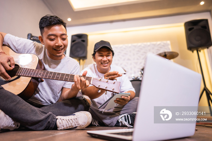 young asian boy playing guitar and his friend watching a music video