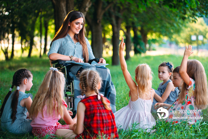 Disabled teacher conducts a lesson with children in nature. Interaction of a teacher in a wheelchair with students.