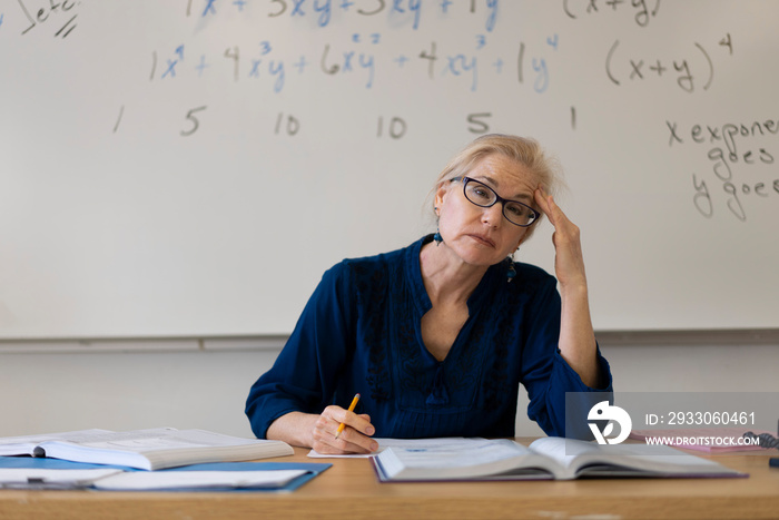 Portrait of frustrated tired high school math teacher sitting on desk talking to students.