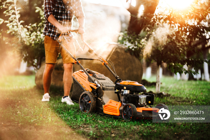 Gardener using industrial lawnmower during summer sunset. Close up details of landscaping and gardening.