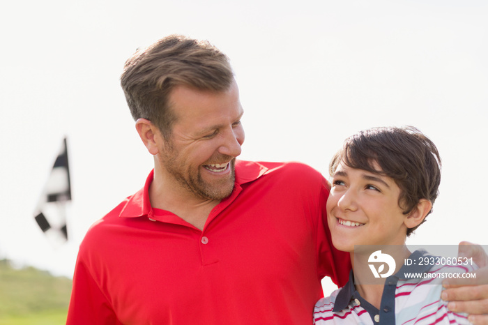 Dad with arm around preteen son on golf course