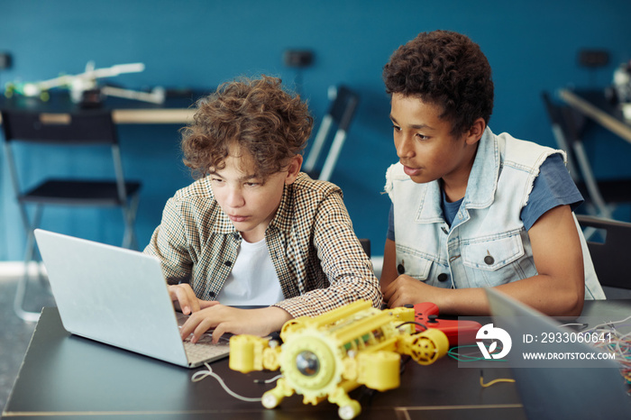 Portrait of two teenage boys using laptop and programming robot during engineering class in school