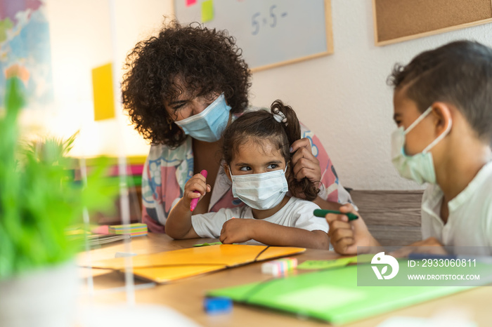 Teacher with children wearing face mask in preschool classroom during corona virus pandemic - Healthcare and education concept