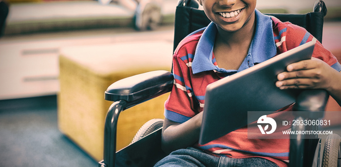 Disabled schoolboy on wheelchair using digital tablet in library