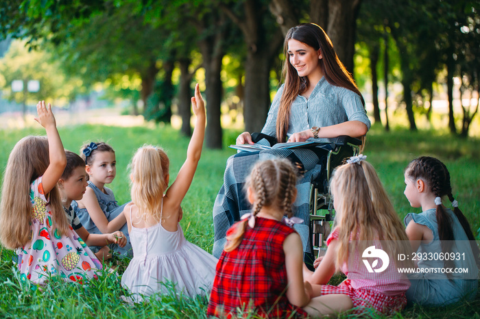 Disabled teacher conducts a lesson with children in nature. Interaction of a teacher in a wheelchair with students.