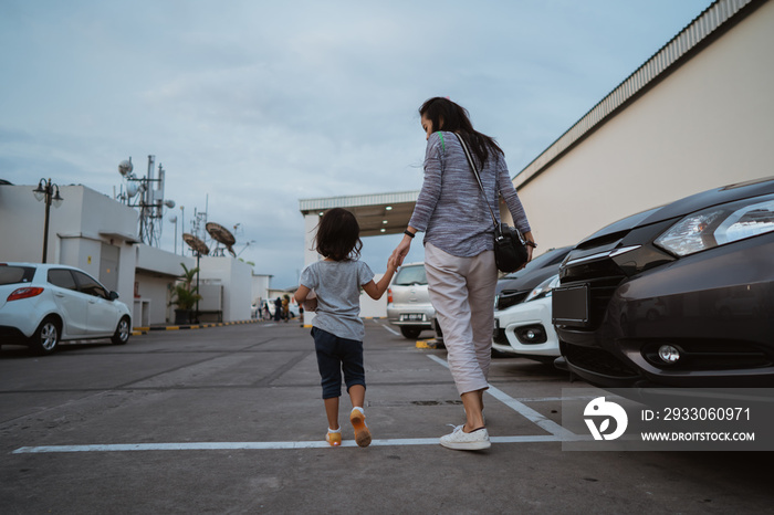 portrait of the mother holding her little daughter hand while walking between the car parks