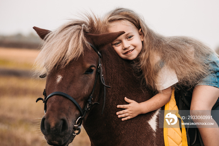 Adorable little girl riding a pony at summer