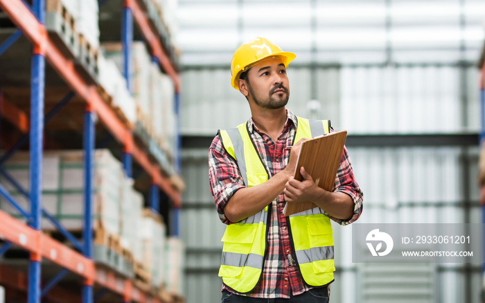 Asian handsome professional male worker holding board, checking shipping stocks in storage, warehouse or factory for delivery, wearing safety hat. Commercial Industry Business Concept.