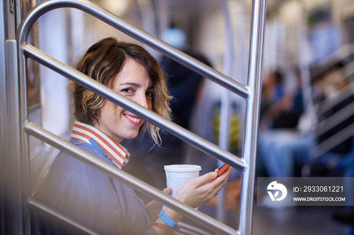 Beautiful young woman travelling in a train of New York underground and drinking coffee