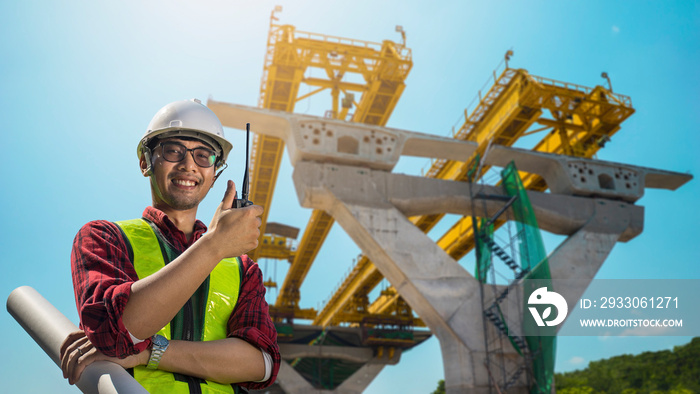 Civil engineer project expressway construction work. Asian young engineer glasses smiling wear a safety helmet equipment and drawing on hand with radio communication.