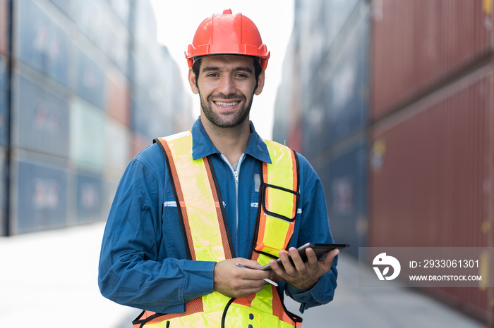 Portrait of foreman container yard worker loading containers box with digital tablet at commercial dock site. Male supervisor checking container at container terminal yard