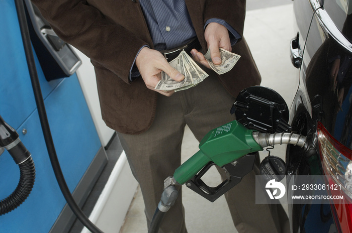 Mid section of man counting money as he refuels car at station