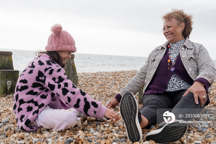 Grandmother and granddaughter sitting on beach on cloudy day