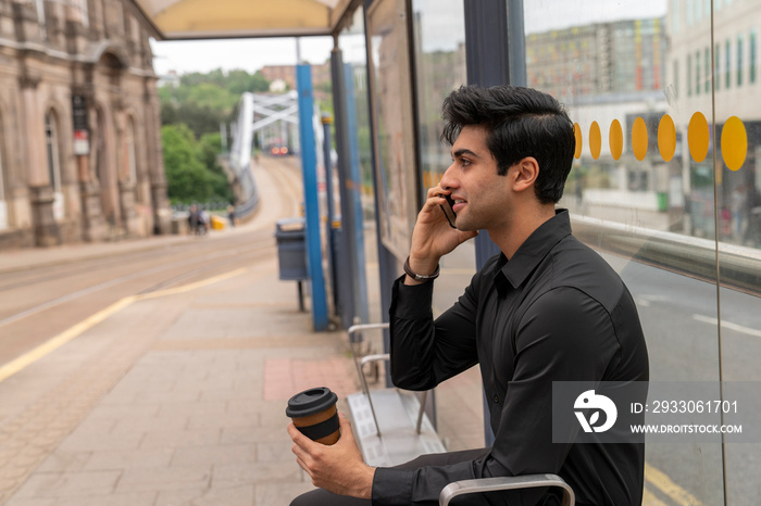 Young man talking by phone on tram stop