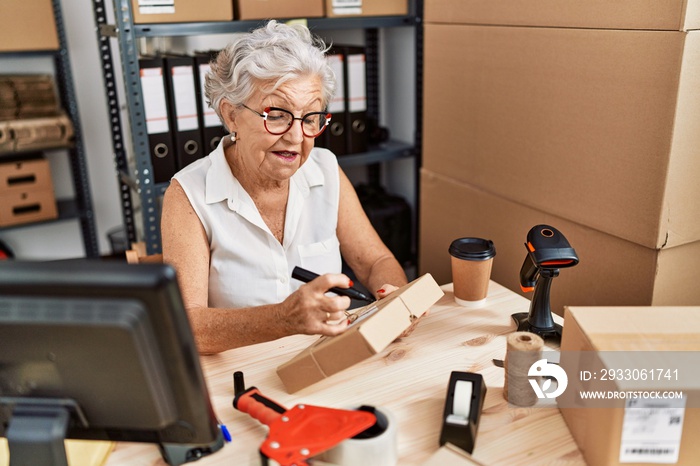 Senior grey-haired woman business worker writing on package order at office