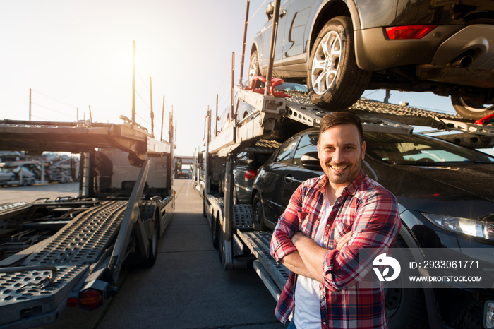 Portrait of truck driver with crossed arms transporting cars to the market. In background truck trailer with cars.