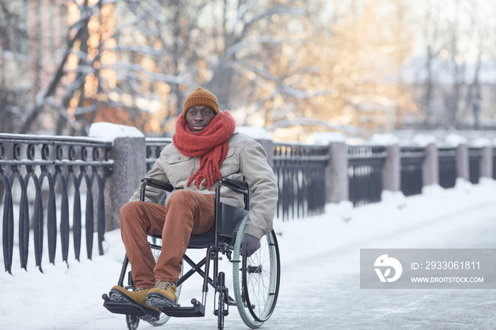 Full length portrait of African American man using wheelchair outdoors in winter and looking at camera , copy space