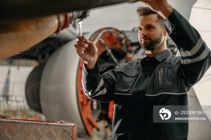 Bearded man maintenance technician using wrench tool while repairing aircraft at repair station