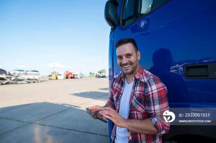 Shot of professional truck driver standing by his truck with tablet computer and setting up GPS navigation for next ride. Transportation services.