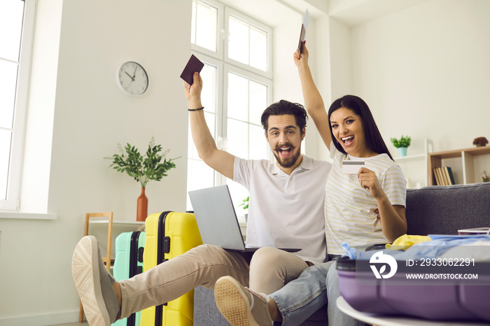 Ready for vacation. Happy young couple in love having fun on couch at home glad they’ve packed travel bags, picked airline online and bought tickets that soon will get them to trip destination abroad