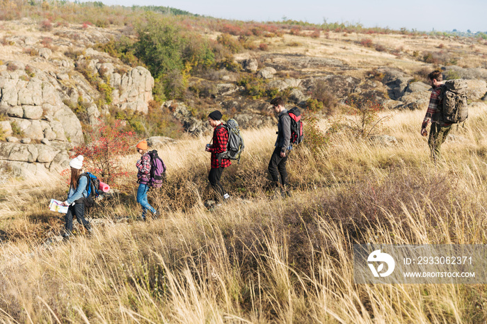 Group of friends outside in free alternative vacation camping over mountains walking with map.