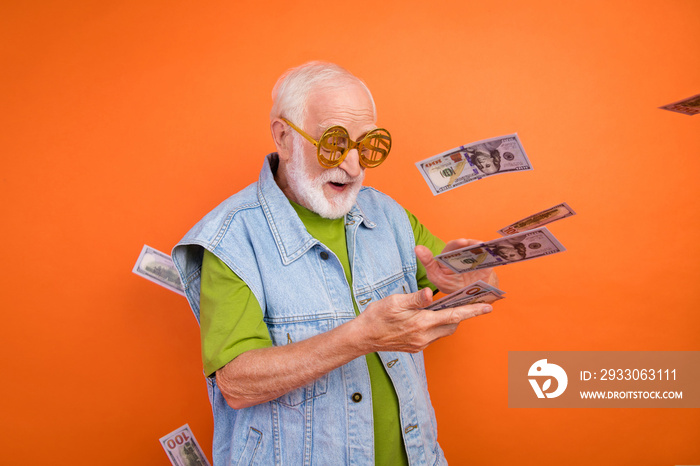 Photo of funny rich retired man wear vintage jeans waistcoat money glasses spending dollars air wind blowing smiling isolated orange color background