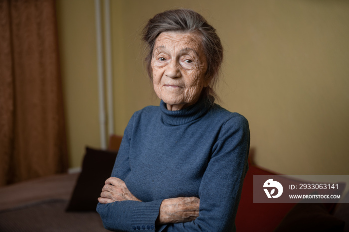 Elderly Caucasian senior grandmother ninety years old looks attentively and smiles, feels happy, large portrait, face with deep wrinkles, gray hair. Theme pensioners, old people and long-lived woman