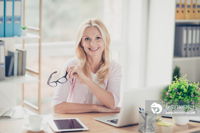 Nice, cute, friendly, aged, experienced financier, holding glasses in hand, having laptop, tablet on the table, looking at camera, sitting at desktop in work place