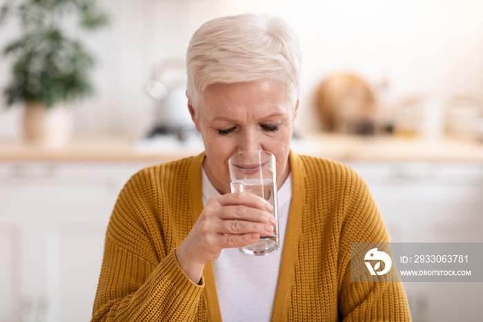 Good looking senior lady drinking still water at home