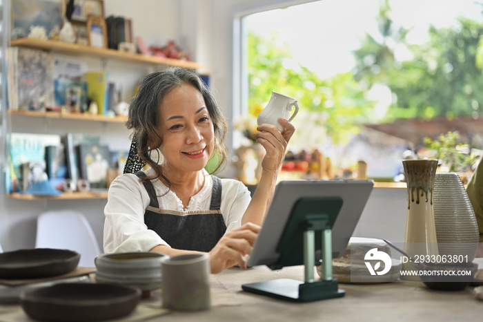 Senior craftswoman with tablet computer in earthenware studio.