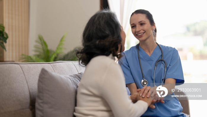 Happy patient is holding caregiver for a hand while spending time together. Elderly woman in nursing home and nurse.