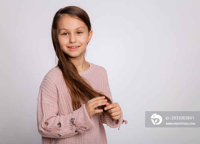 Portrait of a happy smiling child girl. Cute 8 years old girl face expression wearing pink sweater isolated over gray background