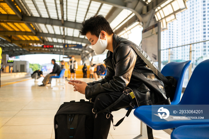 image of asian man sitting and using mobile phone at train station platform