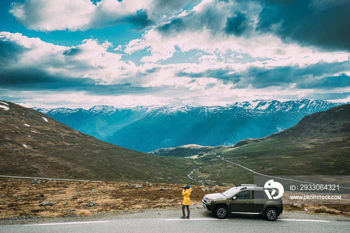 Aurlandsfjellet, Norway. Young Caucasian Woman Lady Tourist Traveler Photographer Taking Pictures Photos Near Parked Car. Aurlandsfjellet Scenic Route Road In Summer Norwegian Countryside Landscape