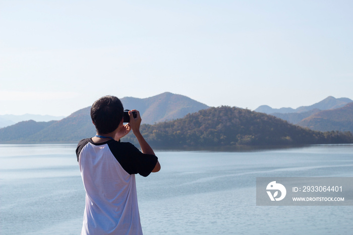 Male tourists are stand taking pictures green forest, mountains and lake view at the Kaeng Krachan National Park, Phetchaburi Thailand.