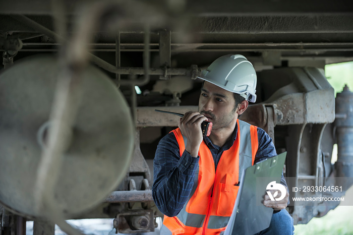 Railroad worker checking up wheels and braking system of freight train. Safety inspector or maintenance engineer checking rail tracks at station. worker service checking  undercarriage of train bogie