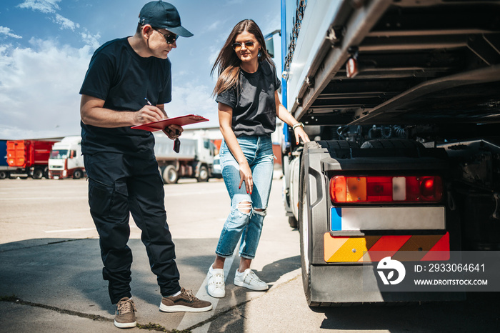 Two professional truck drivers stand in front of the big truck. They talk and perform a technical inspection of the vehicle before next drive. Professional transportation concept.