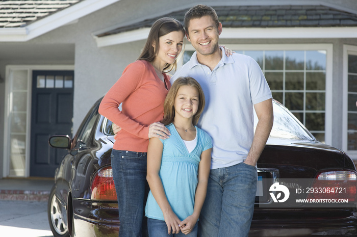 Portrait of a happy couple with daughter standing against car and house