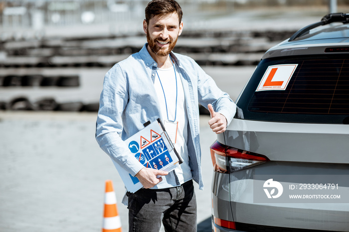 Portrait of a handsome drivers instructor standing with road signs near the learning car on the training ground outdoors