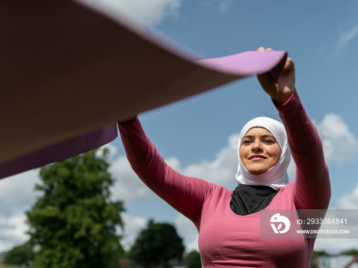 UK,Sutton,Woman in headscarf unrolling yoga mat outdoors