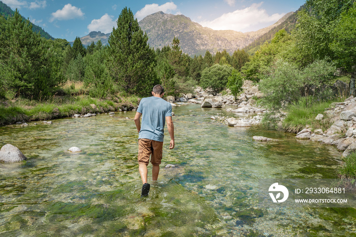 Young man walking inside the river in a beautiful  landscape during the sunset. Natural and wild lifestyle Relax, disconnection and freedom concept. Travel and vacations concept.