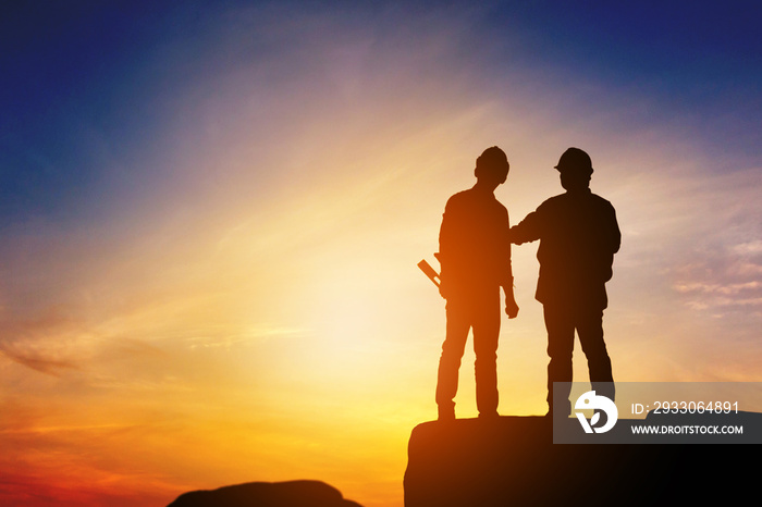 Silhouette of Engineer and worker standing on stone thinking of project sunset in evening time.