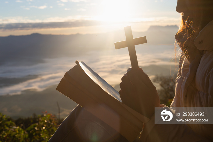 Women pray to God with the Bible and the cross on the mountain background with morning sunrise. Woman Pray for god blessing to wishing have a better life. Christian life crisis prayer to god.