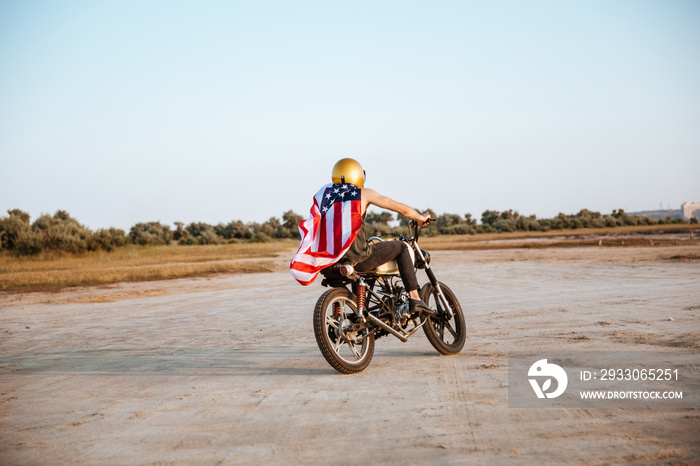 Man in golden helmet and american flag cape driving motorcycle