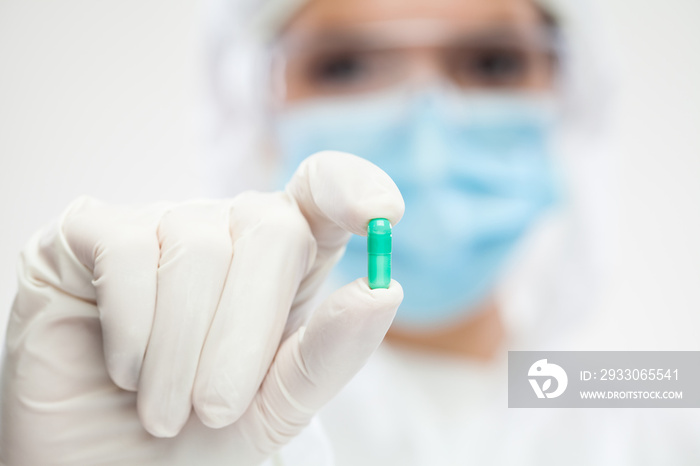 Female pharmacist wearing PPE personal protective equipment holding green pill