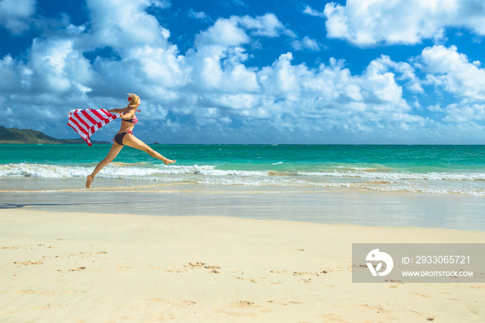 Patriotic woman american bikini weaving american flag. Female jumping in tropical Hawaiian beach. Lanikai Beach in Oahu, Hawaii, USA. Freedom and 4th July patriotic concept in Indipendence day.