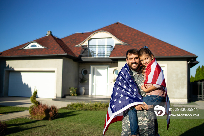 Portrait of father soldier on military leave holding his lovely daughter in front of their house.