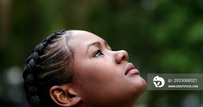 Hopeful African woman standing outside looking at sky in contemplation